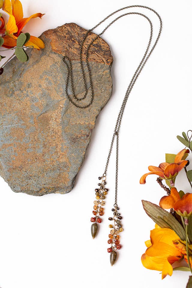 Handcrafted Fireside Collection Lariat Necklace laid on a stone surface, showcasing the warm tones of cat's eye, Czech glass, and labradorite gemstones with a mixed metal chain.