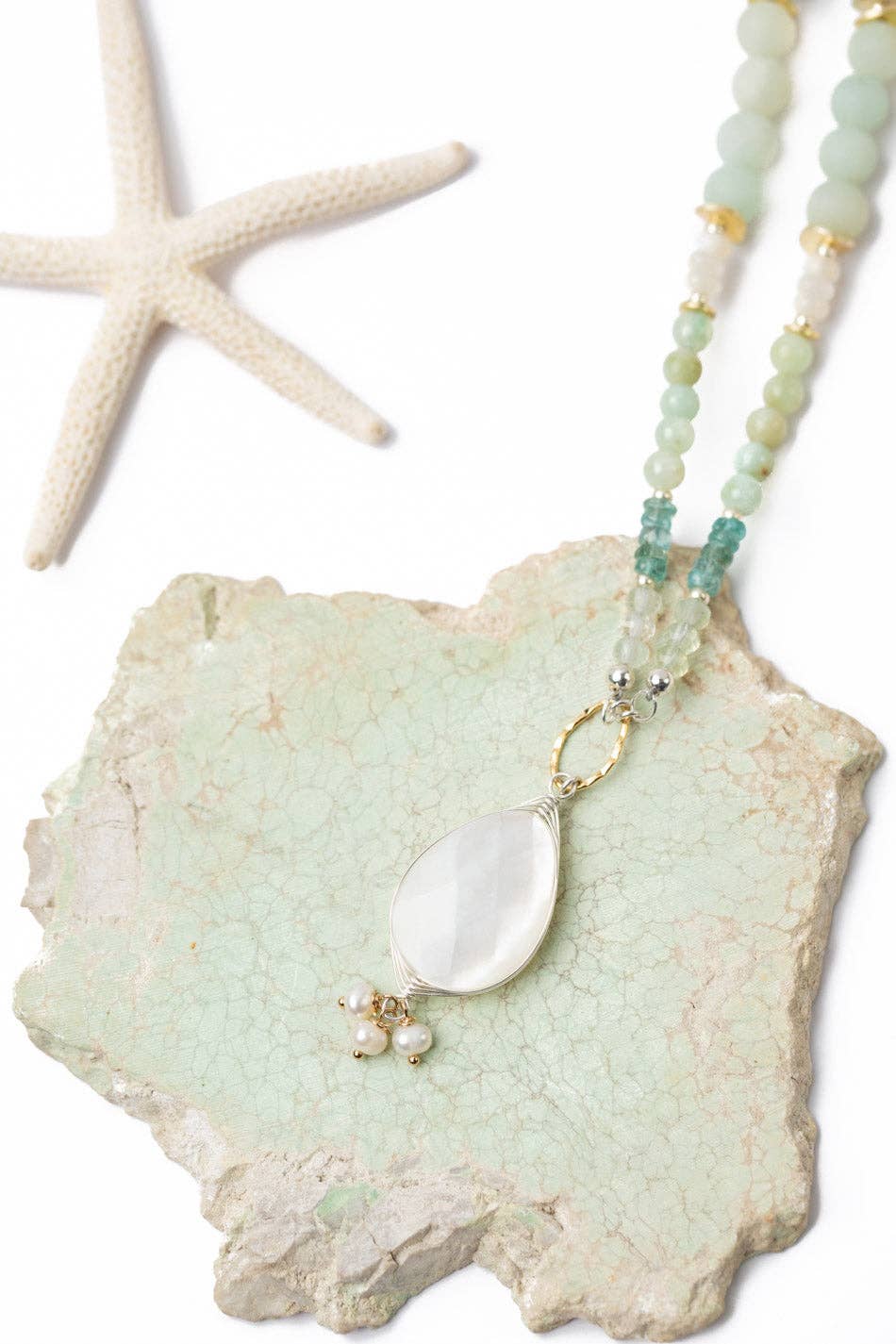 A close-up of the mother of pearl pendant and the surrounding freshwater pearls, amazonite, and blue apatite beads, emphasizing the intricate craftsmanship and serene color palette.