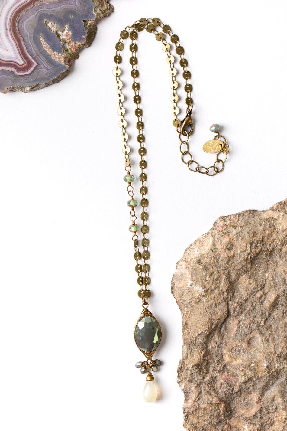 Herringbone Wrapped Crystal Focal Necklace laid flat on a white background with rocks, showcasing the antique brass chain and hand-wrapped crystal focal.