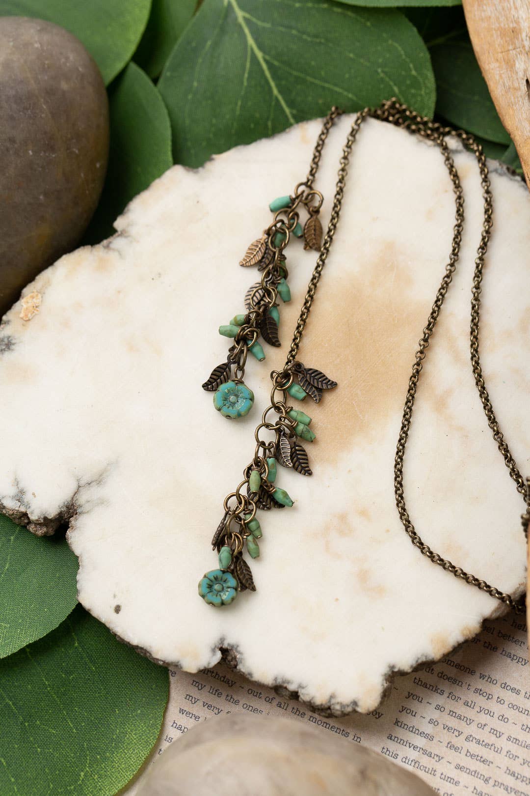 A close-up of the Turquoise and Czech Glass Lariat Necklace, highlighting the intricate beadwork and antique brass leaf charms against a white marble background.