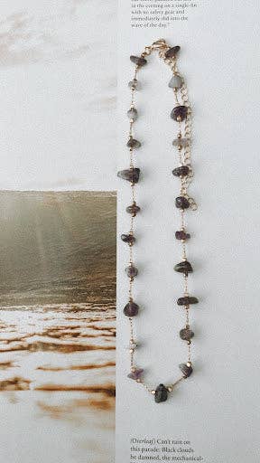 A Purple Rain Choker featuring amethyst chip beads and a 14k gold-plated stainless-steel chain, displayed on a light background with a scenic backdrop.