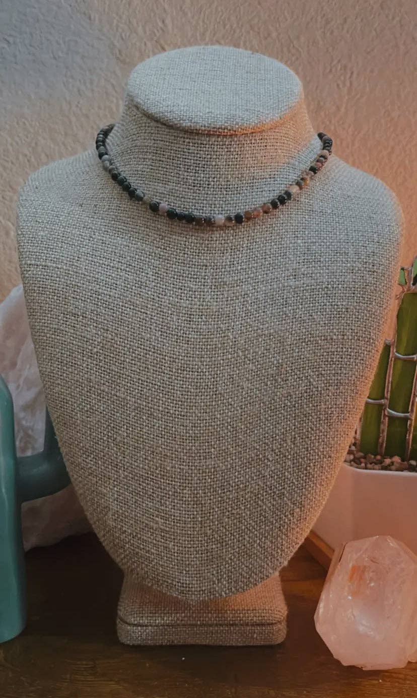 A Pink Tourmaline Choker featuring 4mm pink tourmaline beads and a 14k gold-plated stainless-steel chain, displayed on a beige fabric bust against a textured background.