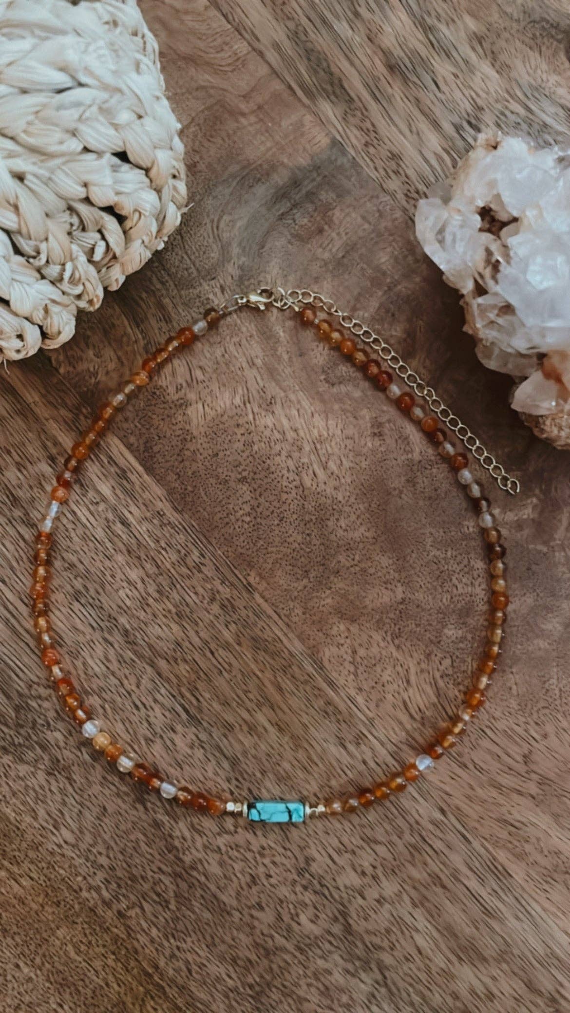 The West Coast Choker featuring vibrant carnelian beads and a striking turquoise tube bead, displayed on a wooden surface, highlighting its adjustable 14-17 inch length and elegant design.